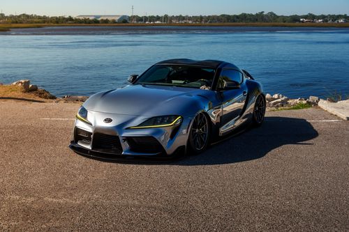 Free Stylish silver sports car parked by a scenic riverside under clear blue skies. Stock Photo