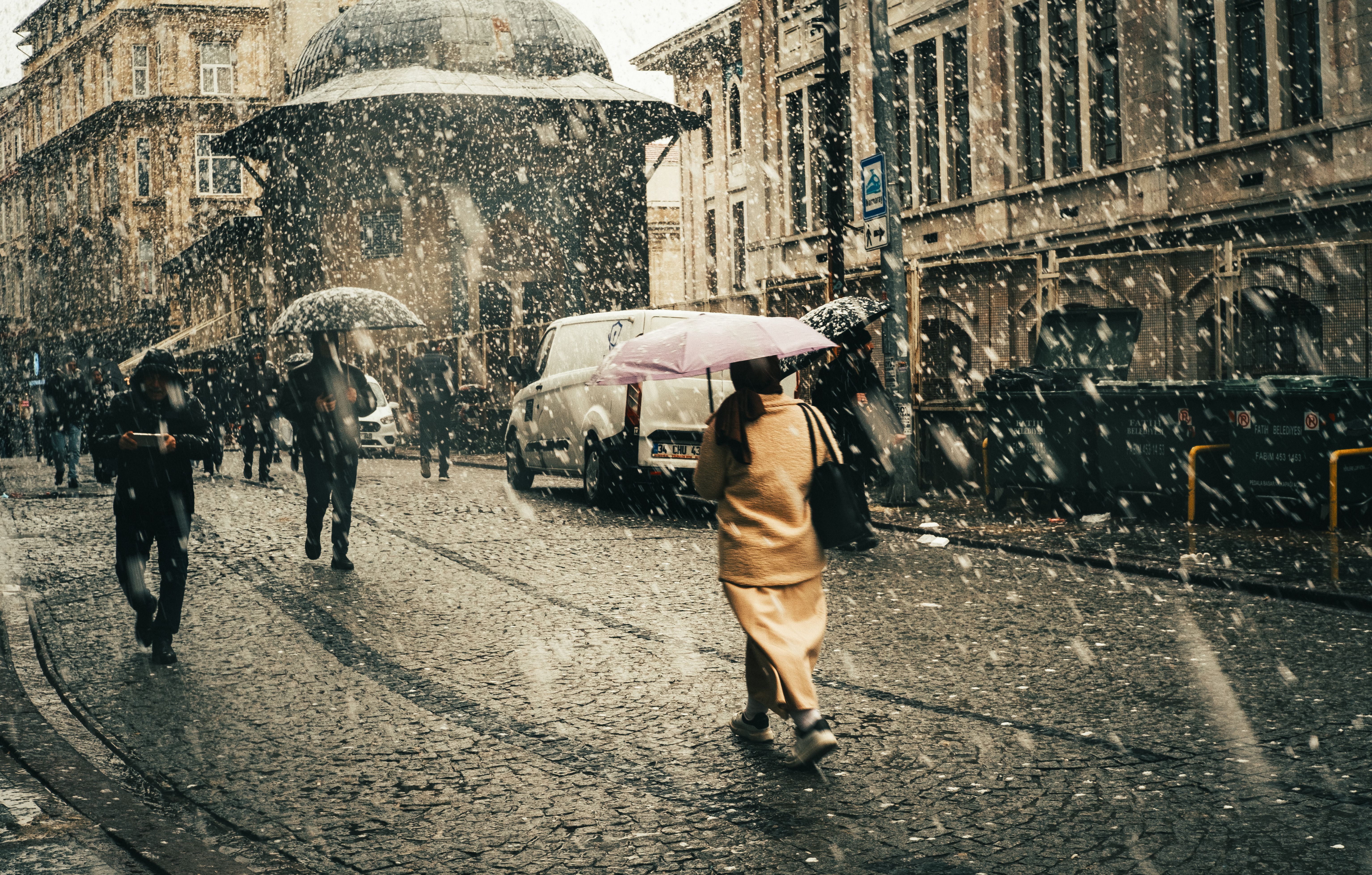 People walk through a snowy street in an urban area, carrying umbrellas.