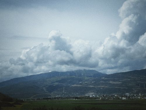 Free Breathtaking view of a cloudy sky over a lush green valley with distant wind turbines. Stock Photo