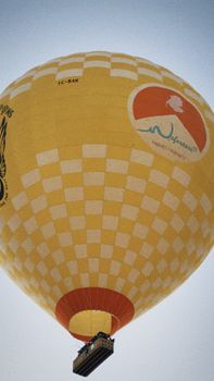 A vibrant yellow hot air balloon with checkered pattern floating in a clear sky.