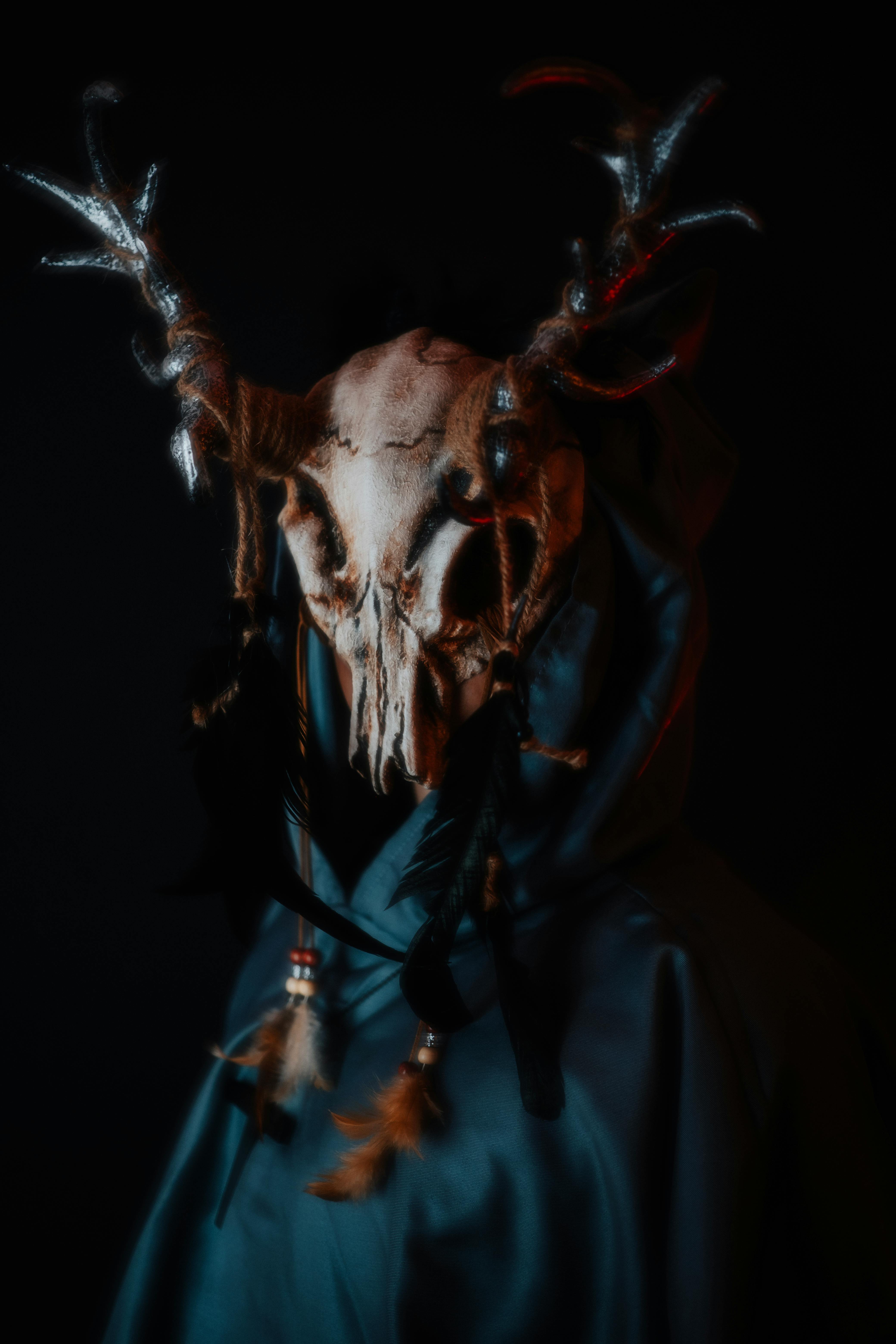 Dark, mystical image of an antlered mask with artistic feathers and a cloak, creating an eerie atmosphere.