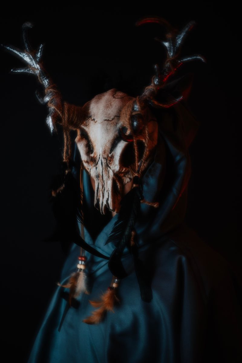 Dark, mystical image of an antlered mask with artistic feathers and a cloak, creating an eerie atmosphere.
