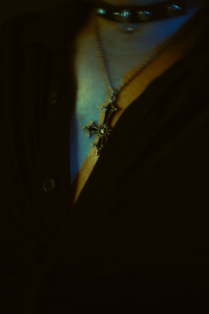 Dark and moody image of a cross pendant on a buttoned shirt, casting a mysterious aura.