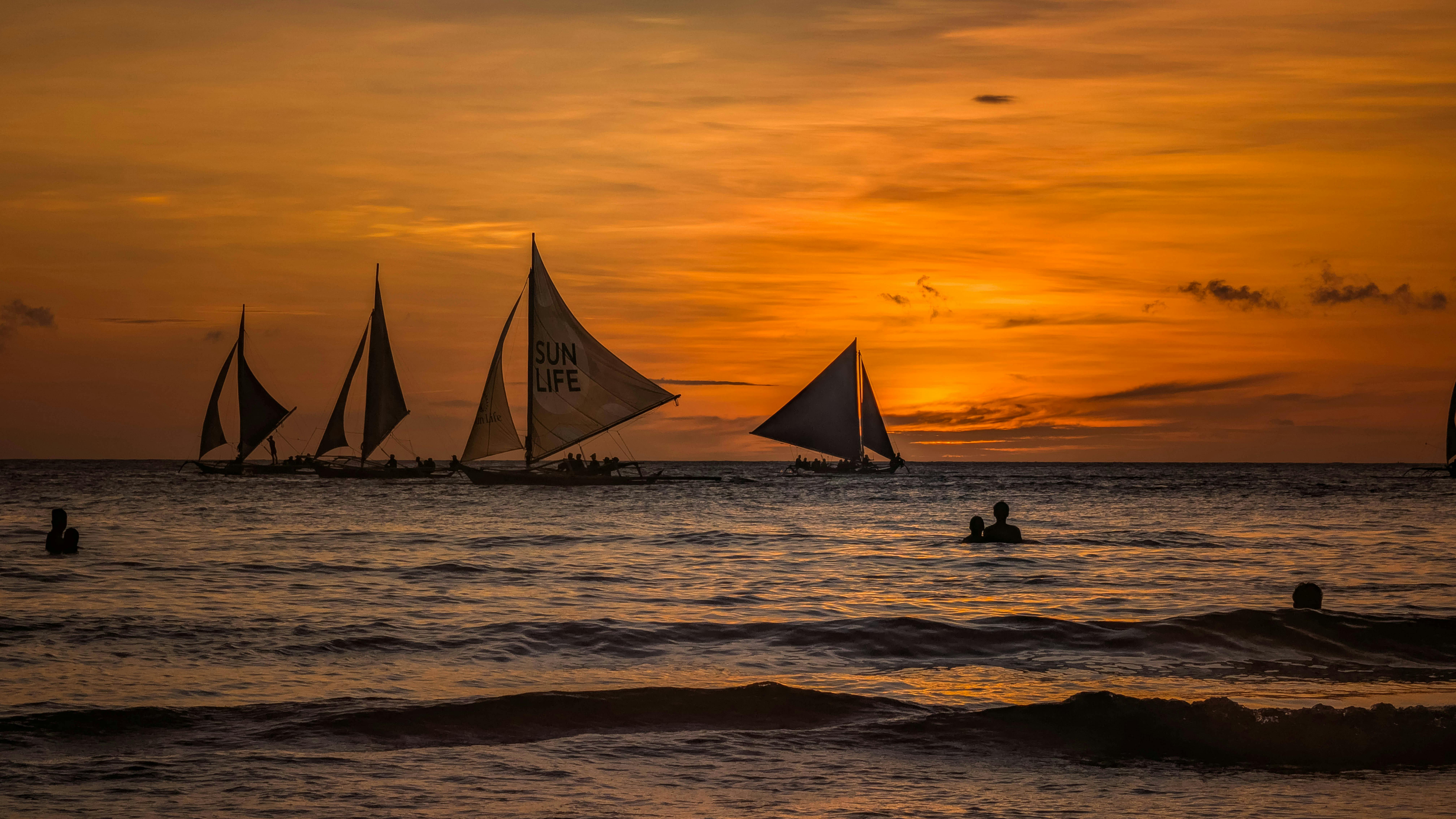Beautiful sunset over the sea in the Philippines with sailboats and silhouettes of people swimming. (Photo: Jane Foster)