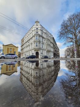 Elegant historic building in Wrocław, Poland reflects in a puddle on a clear day.