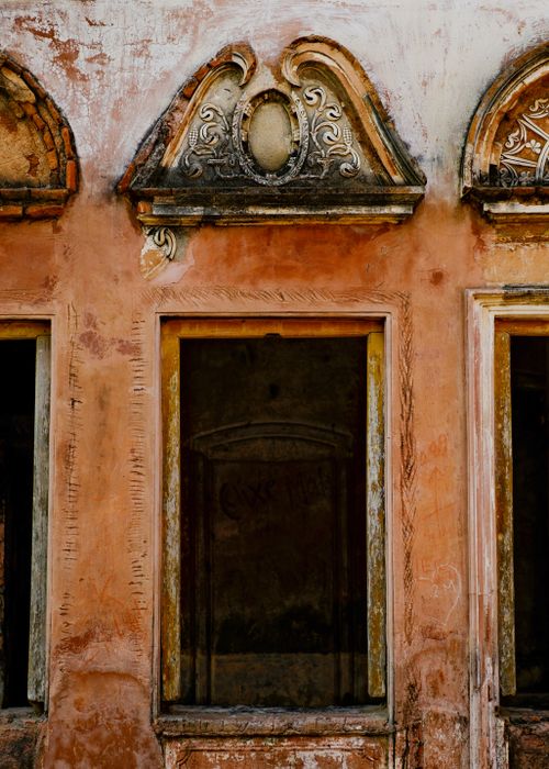 Free Close-up of an ornate, weathered window facade with detailed carvings and faded paint, showing classic architectural style. Stock Photo