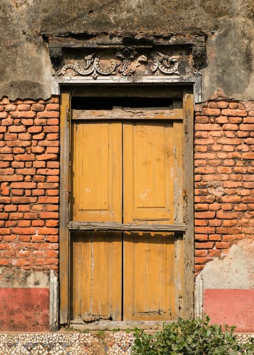 Free A rustic yellow wooden door with ornate details set in a weathered brick wall, highlighting urban decay. Stock Photo