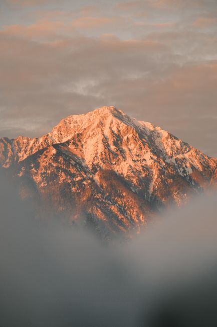 Breathtaking view of a snow-capped mountain at sunset with clouds in the foreground.