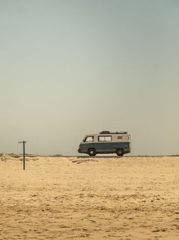 A classic camper van parked on a remote sandy beach under a clear sky, perfect for travel inspiration.