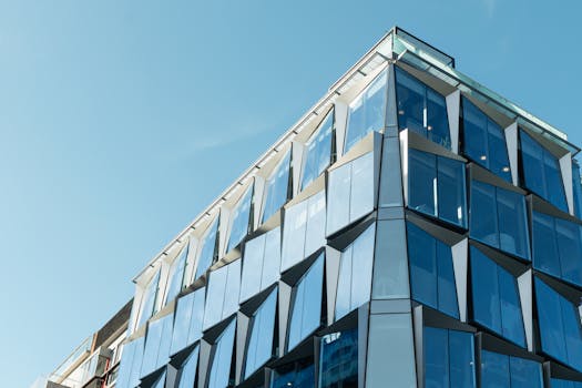 A modern architectural building with glass facades reflecting a clear blue sky. Ideal for urban and architectural themes.