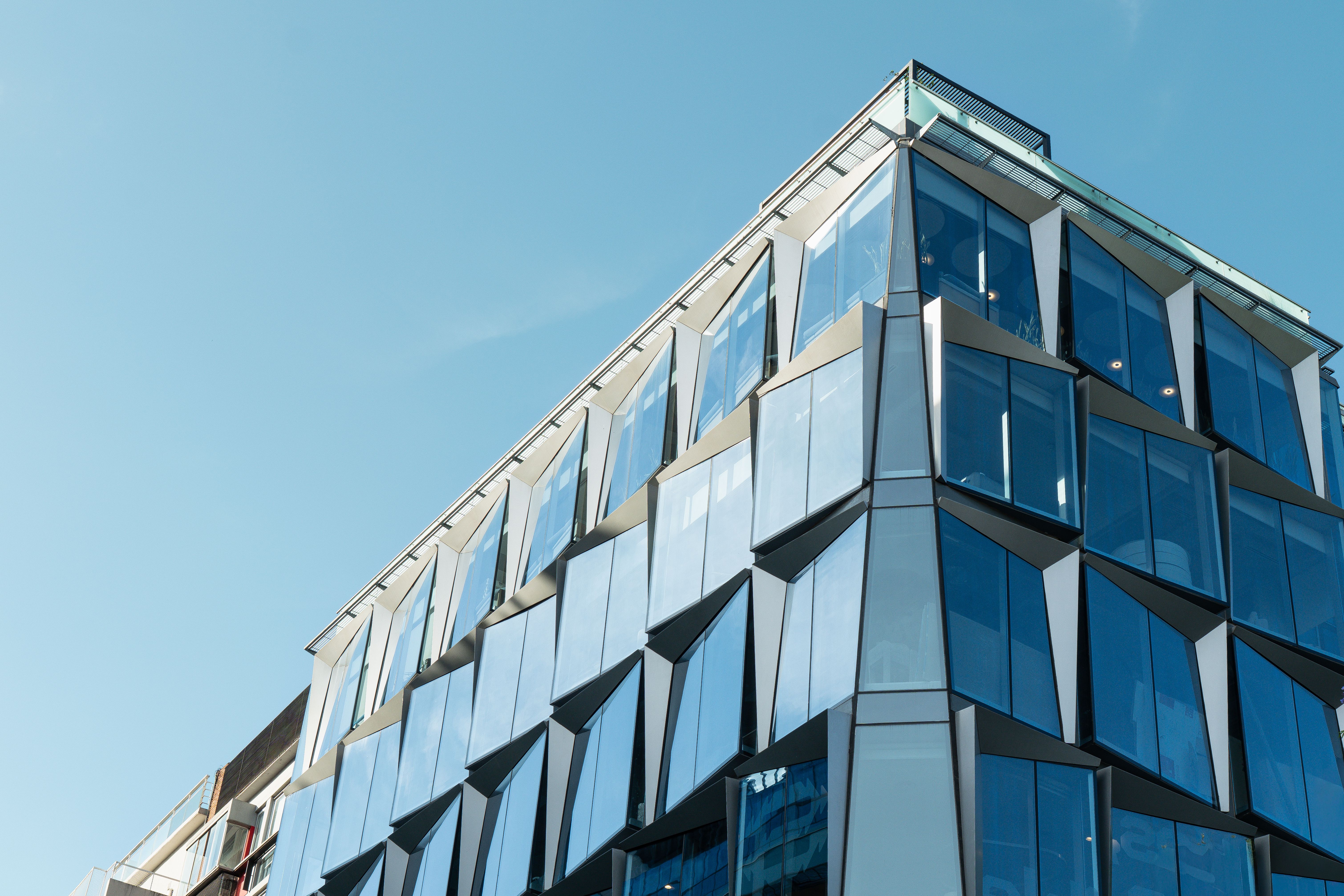 Gratis En moderne arkitektonisk bygning med glassfasader som reflekterer en klar blå himmel. Ideell for urbane og arkitektoniske temaer. Arkivbilde