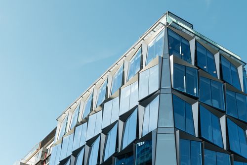 Gratis En moderne arkitektonisk bygning med glassfasader som reflekterer en klar blå himmel. Ideell for urbane og arkitektoniske temaer. Arkivbilde
