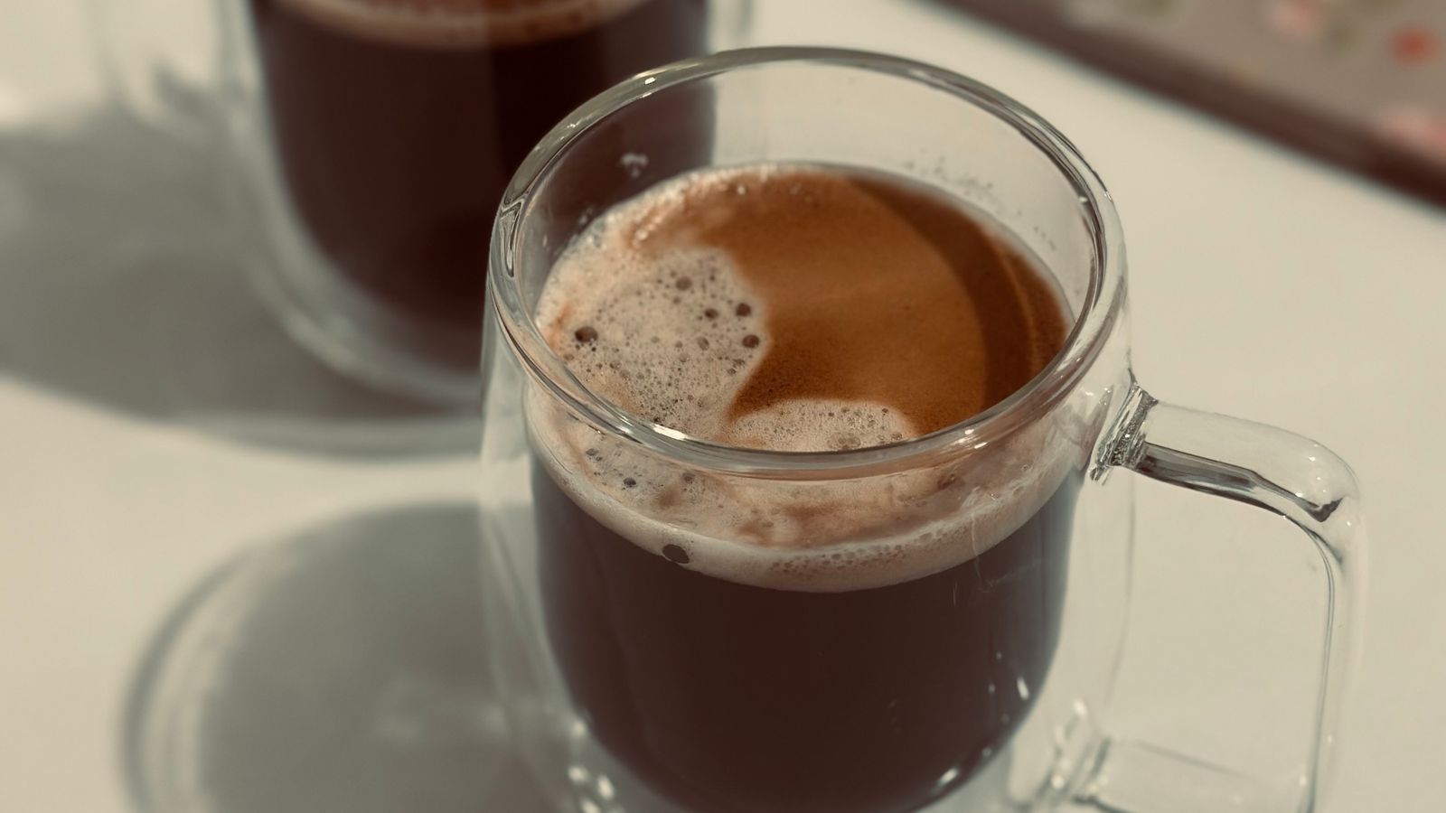 Two glass mugs of coffee on a light table