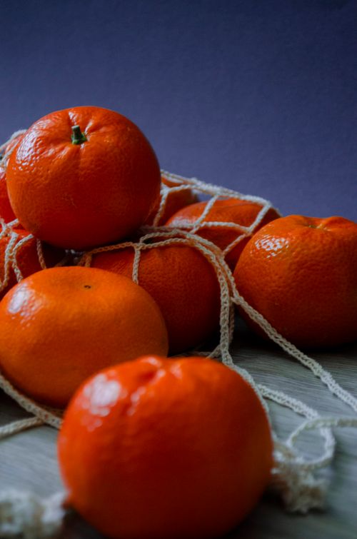 Free Bright orange mandarins lying in a string bag against a deep blue background. Stock Photo