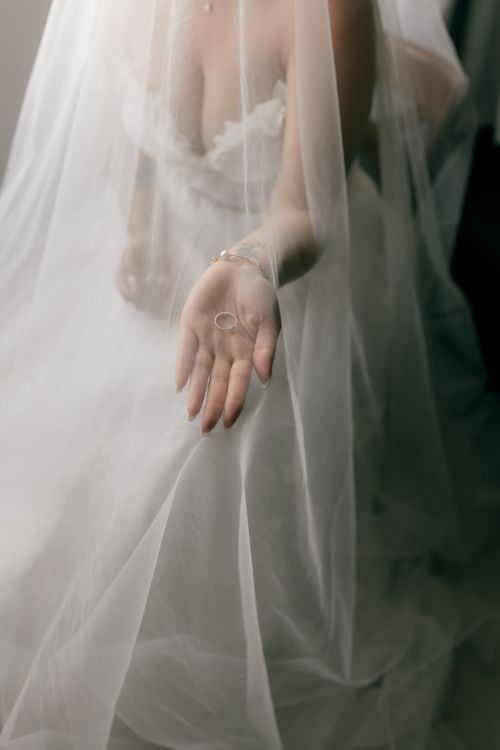 Free A bride in a sheer white gown gracefully holds a wedding ring beneath her veil, symbolizing eternal love and commitment. Stock Photo