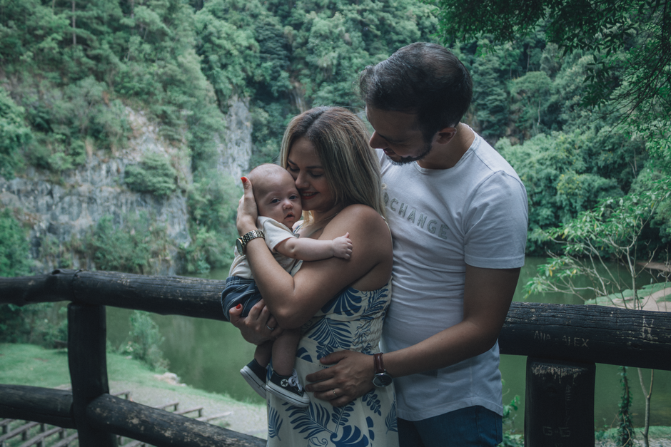 A family enjoys a tender moment outdoors by a cliffside, cuddling their baby in a serene natural setting.