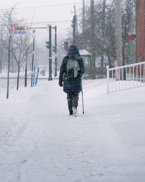 Free A person walks through a snowy street in Longueuil, Quebec, capturing the essence of winter urban life. Stock Photo