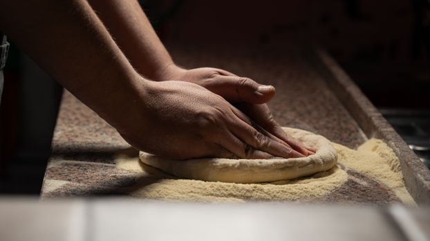 Close-up of hands kneading pizza dough on a floured countertop, indoors.