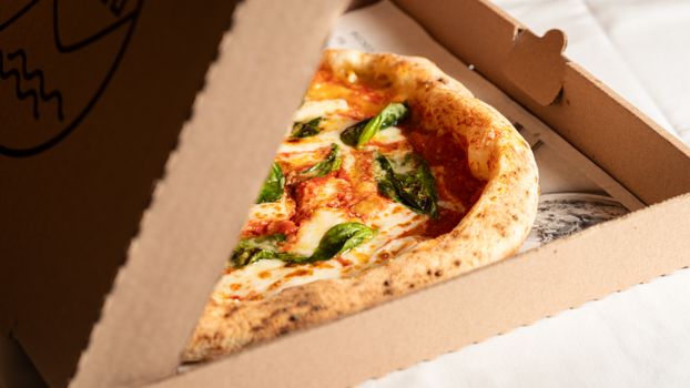 Delicious Margherita pizza with fresh basil in a cardboard box, ready to serve.