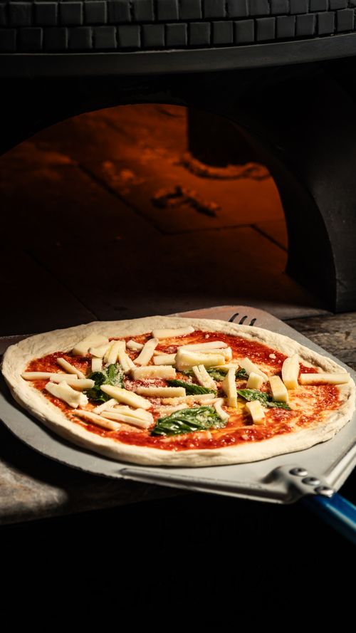 Free Delicious margherita pizza on a peel ready to bake in a traditional wood-fired oven. Stock Photo