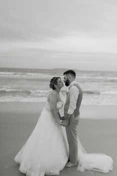 A couple shares a tender kiss on a beach during their wedding at sunset.