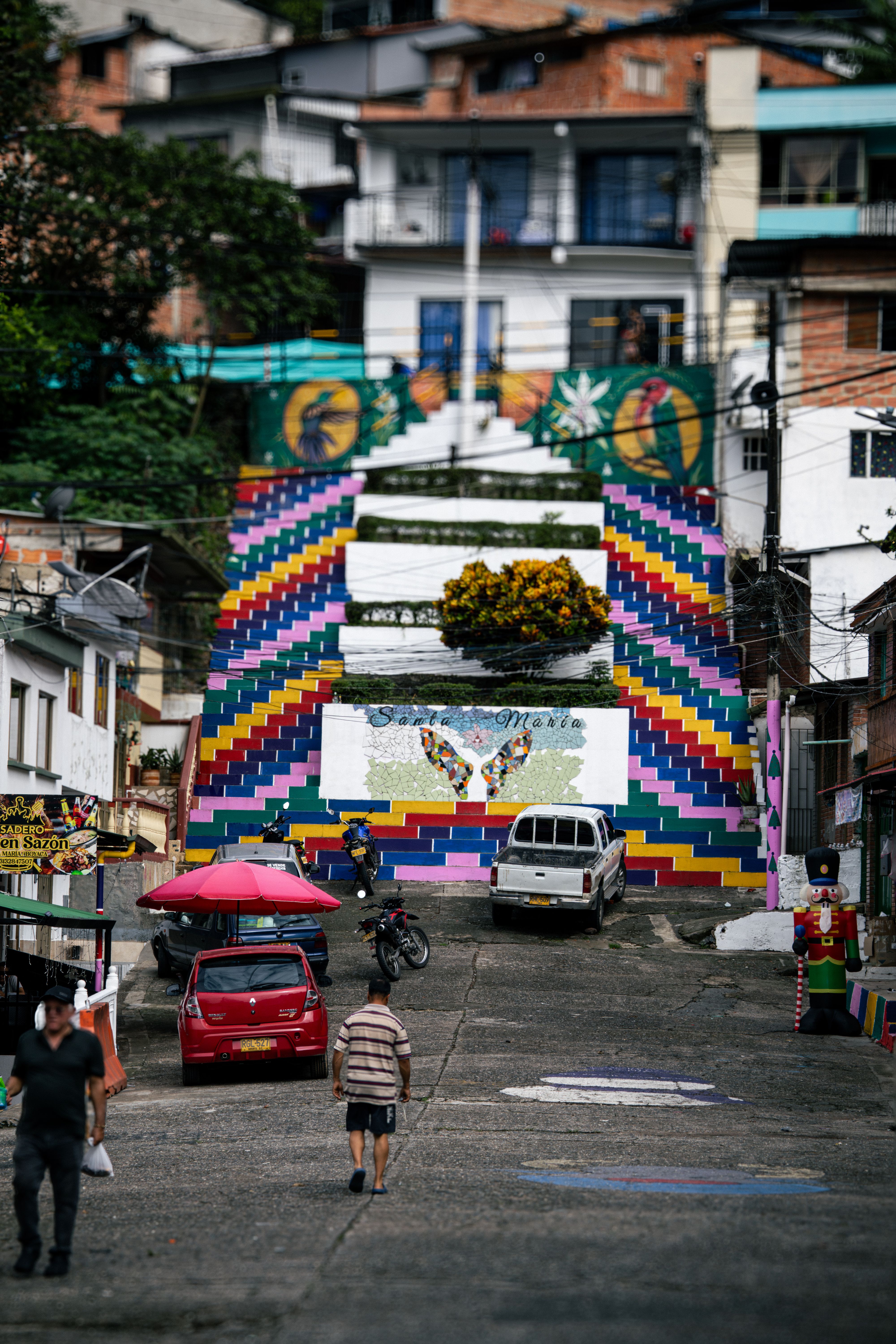 Fotomural Escaleras pintadas de colores vibrantes que conducen a casas en la ladera de una zona urbana y muestran la cultura local.