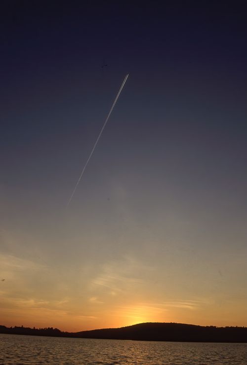 Free Beautiful sunset with a jet contrail streaking across the sky above a calm body of water. Stock Photo