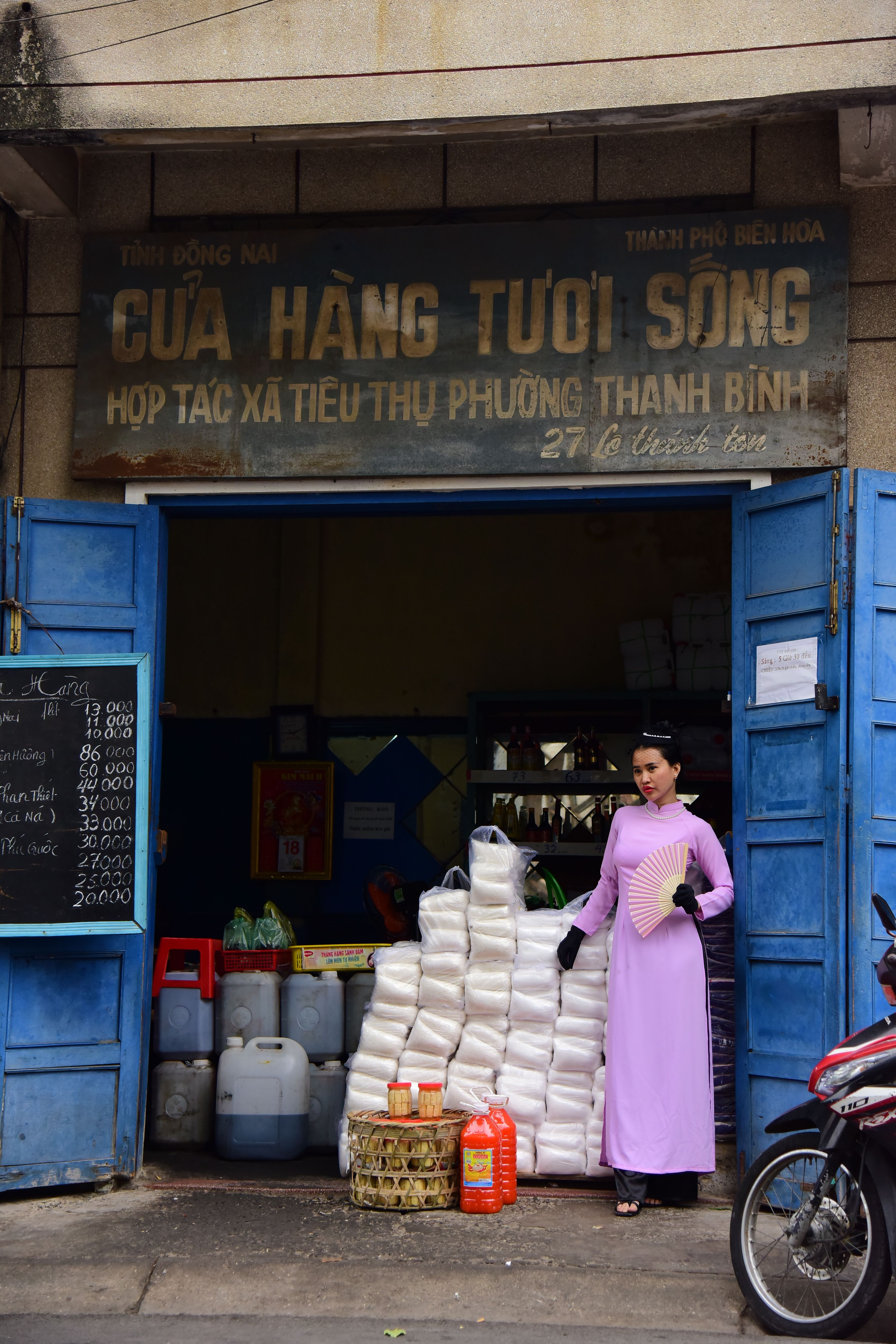 A vendor in traditional attire stands by supplies at a Vietnamese market.