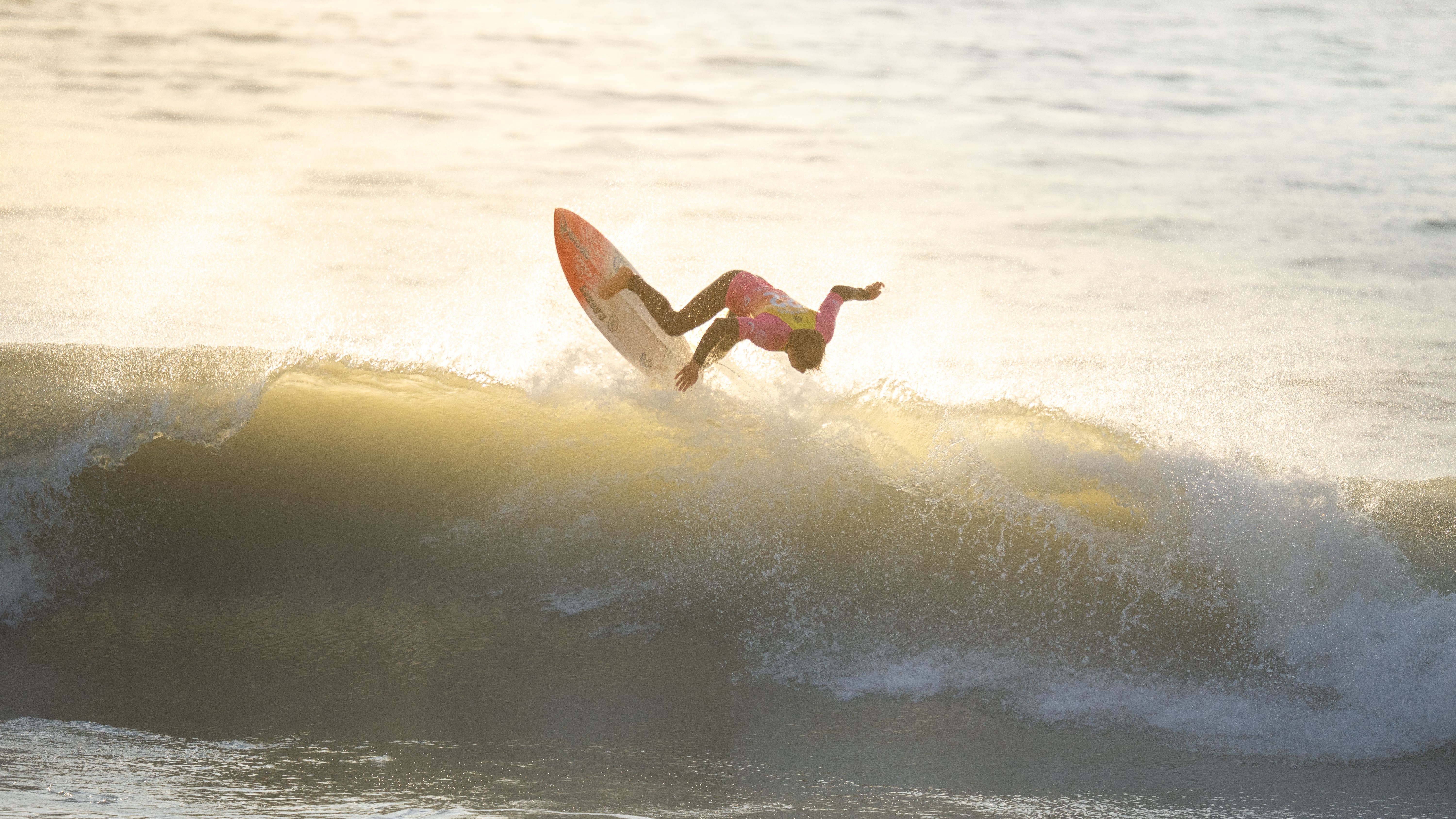 A surfer performing a high-flying move on a wave during sunrise.