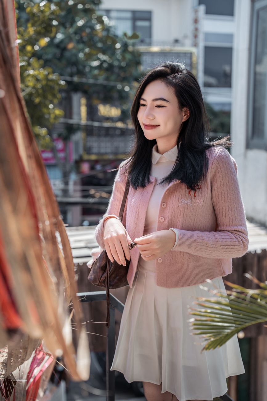 Young woman in pink cardigan smiles outdoors on a sunny day, exuding warmth and cheerfulness.