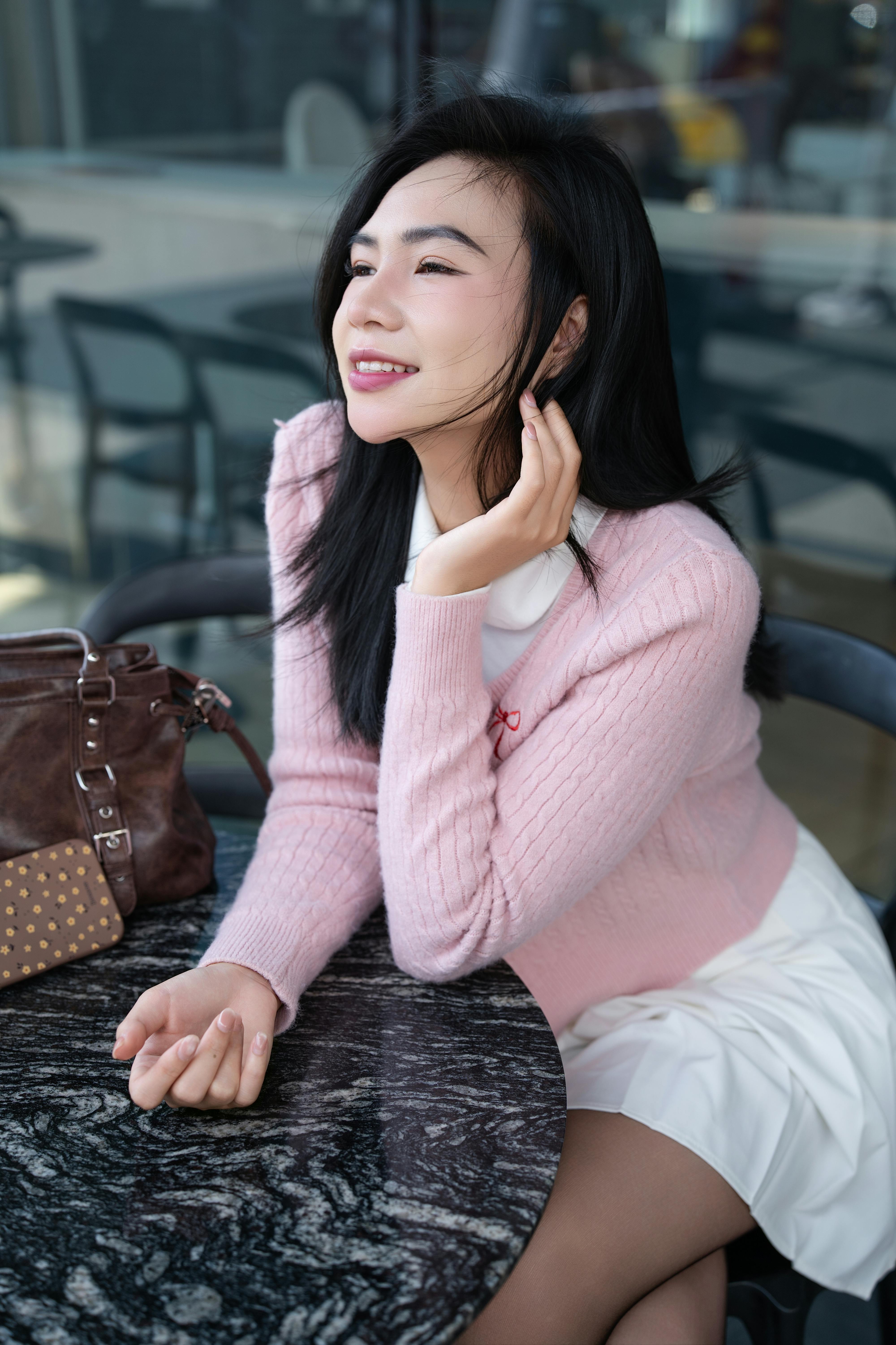 Young woman in a pink sweater sitting at an outdoor cafe, smiling and looking relaxed.
