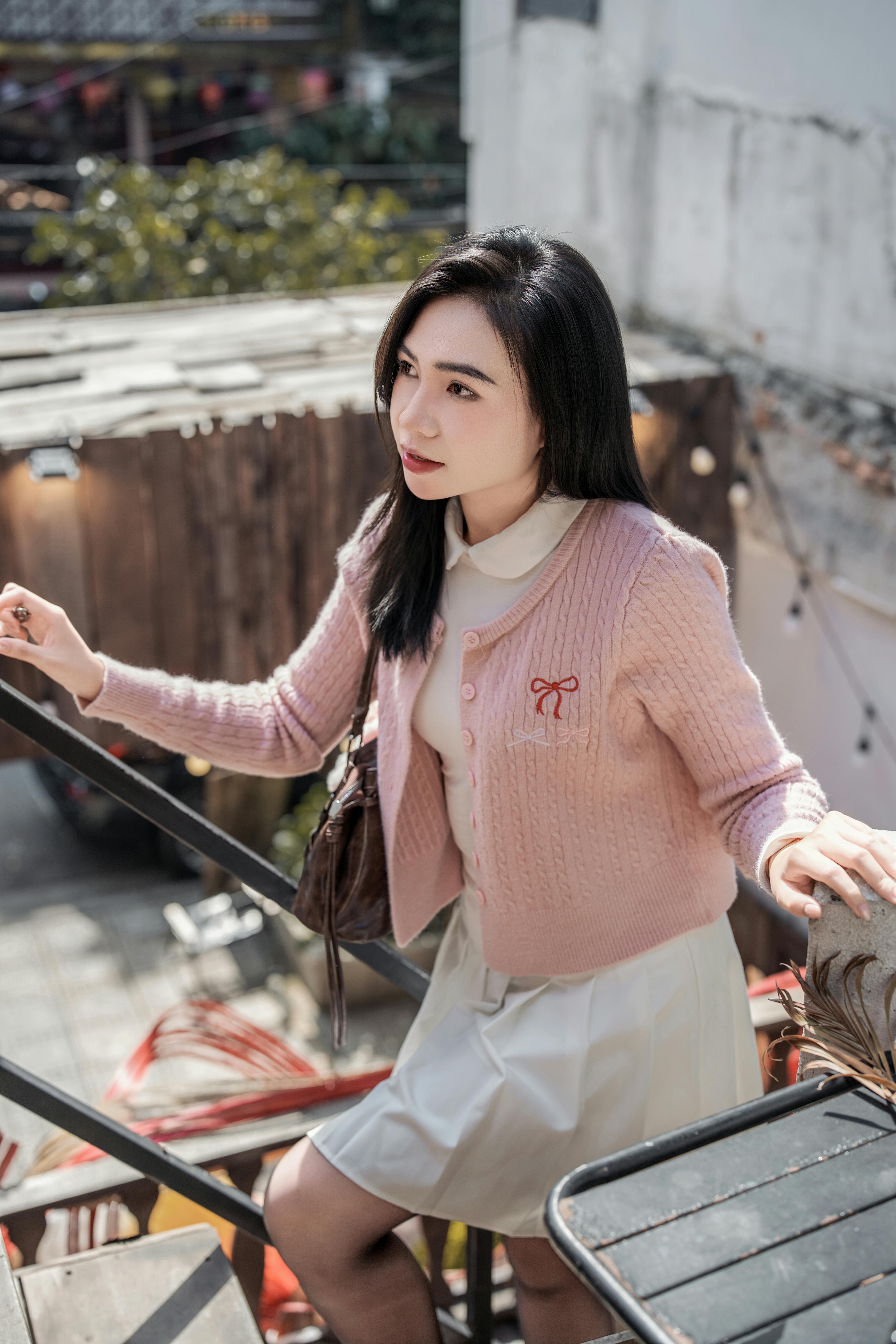 Charming woman in a pink cardigan enjoying a sunny day outdoors, captured in a serene moment.