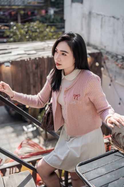 Charming woman in a pink cardigan enjoying a sunny day outdoors, captured in a serene moment.
