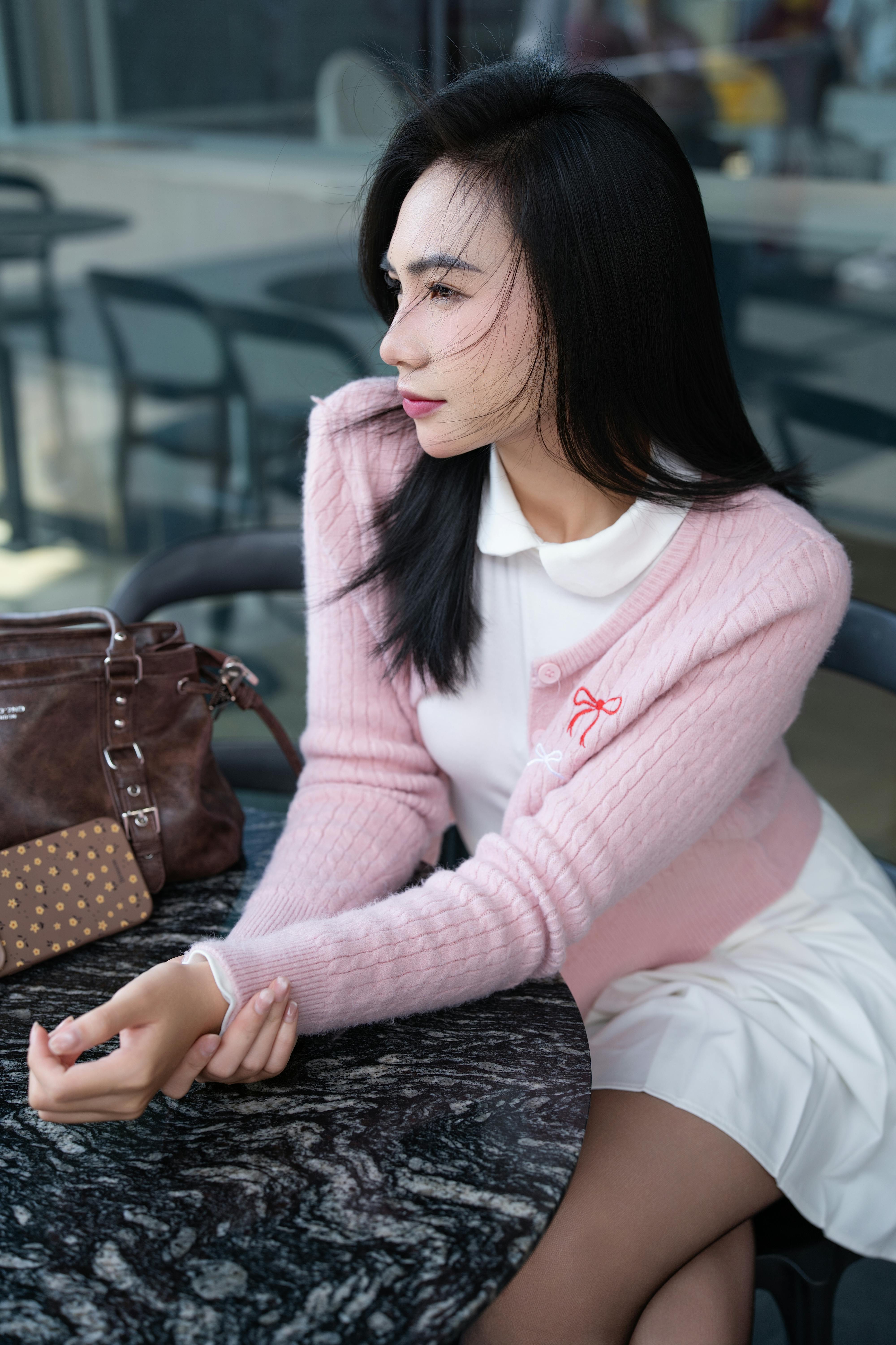 Elegant woman in pink sweater relaxing at a cafe table on a sunny day.