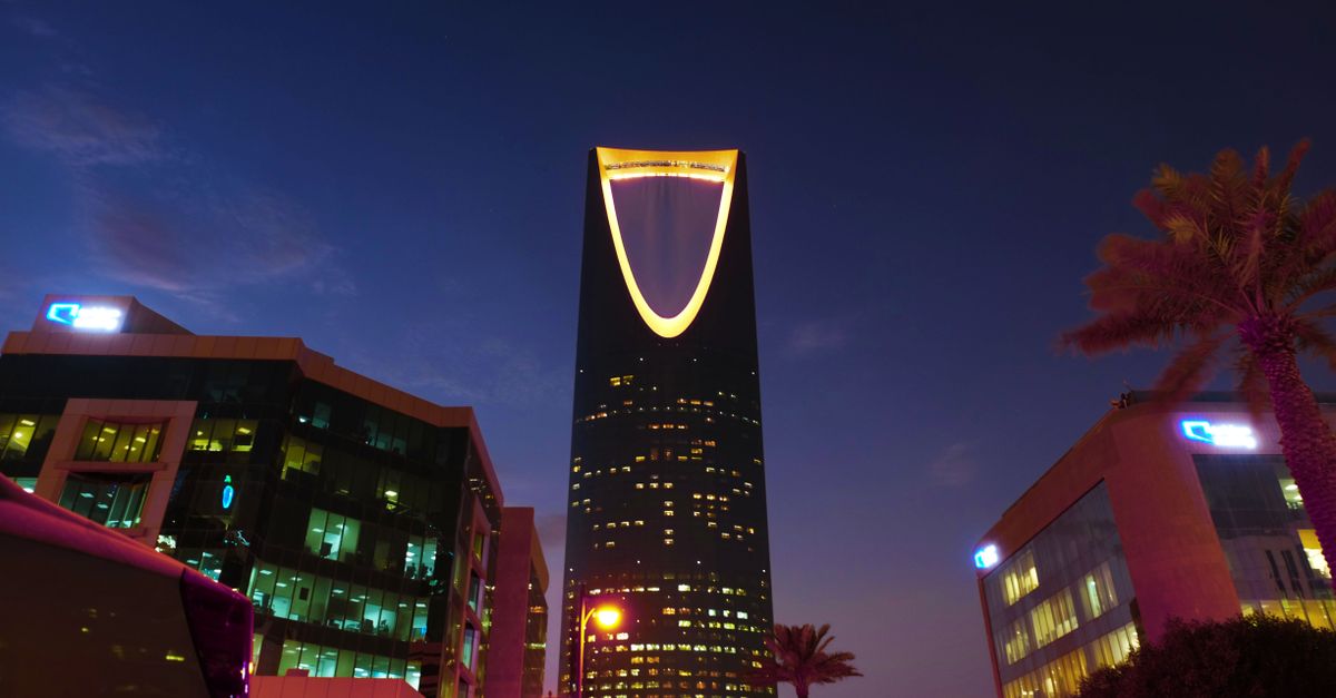 Illuminated Kingdom Centre Tower rises in Riyadh's urban landscape at twilight.