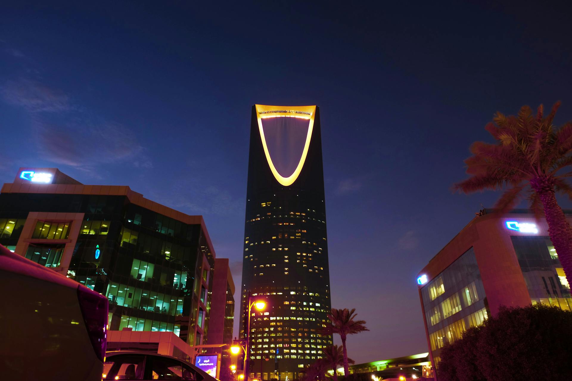 Illuminated Kingdom Centre Tower rises in Riyadh's urban landscape at twilight.