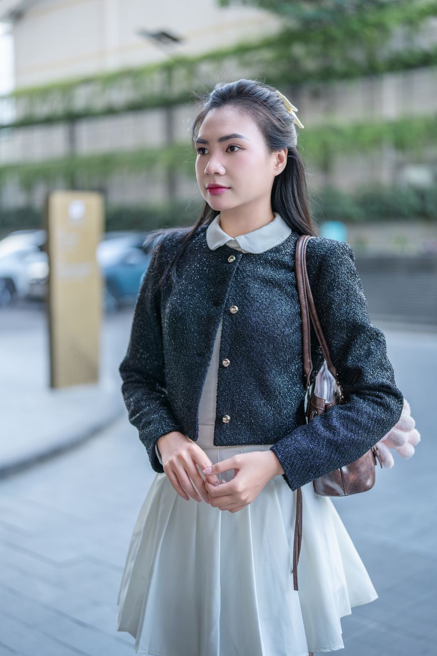 Stylish woman outdoors in a chic jacket and dress with soft lighting.