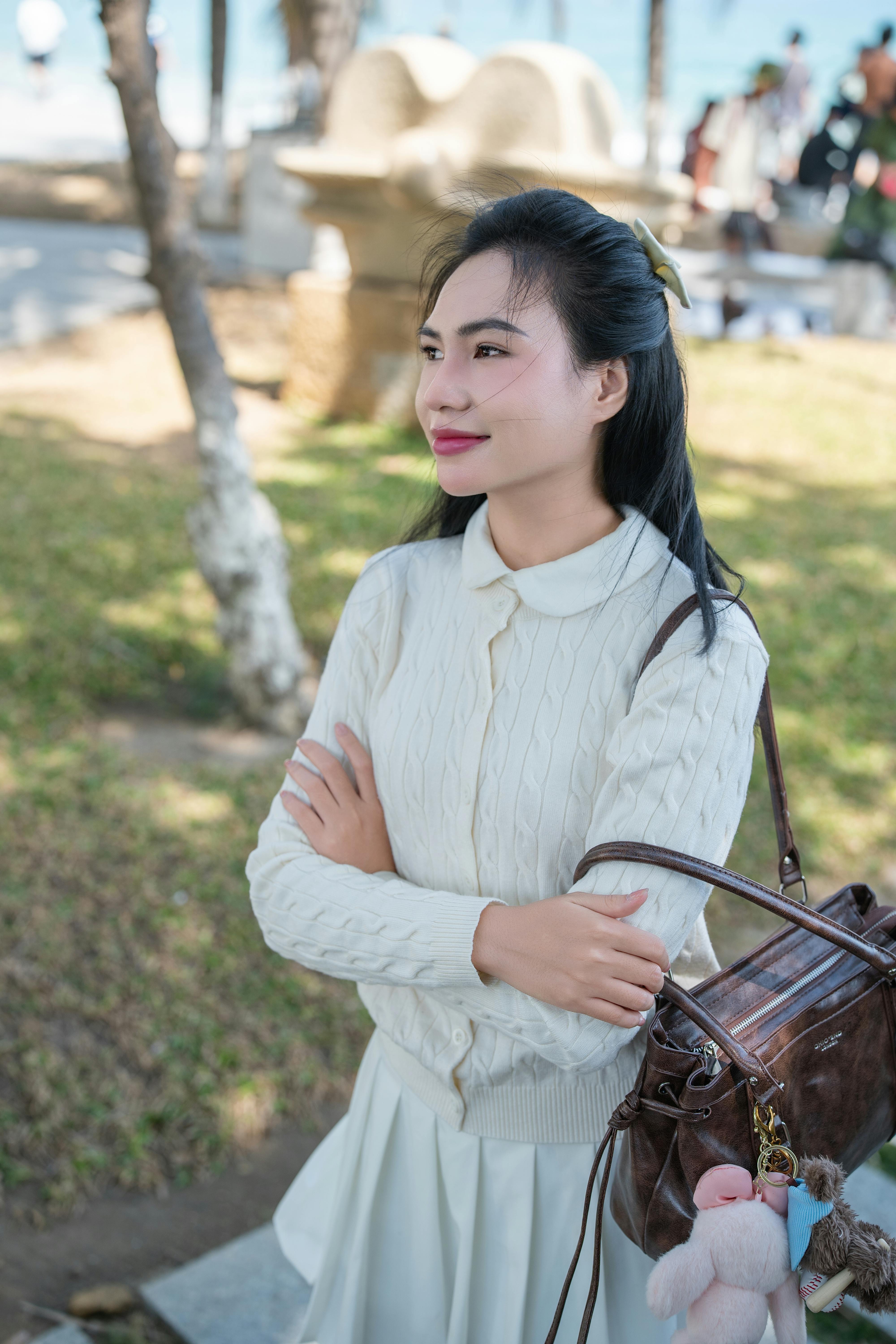 A woman in a white sweater enjoys a sunny day in a park, looking content and relaxed.