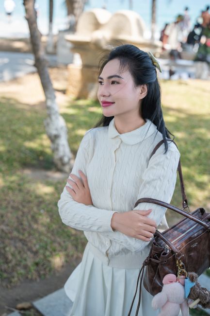 A woman in a white sweater enjoys a sunny day in a park, looking content and relaxed.