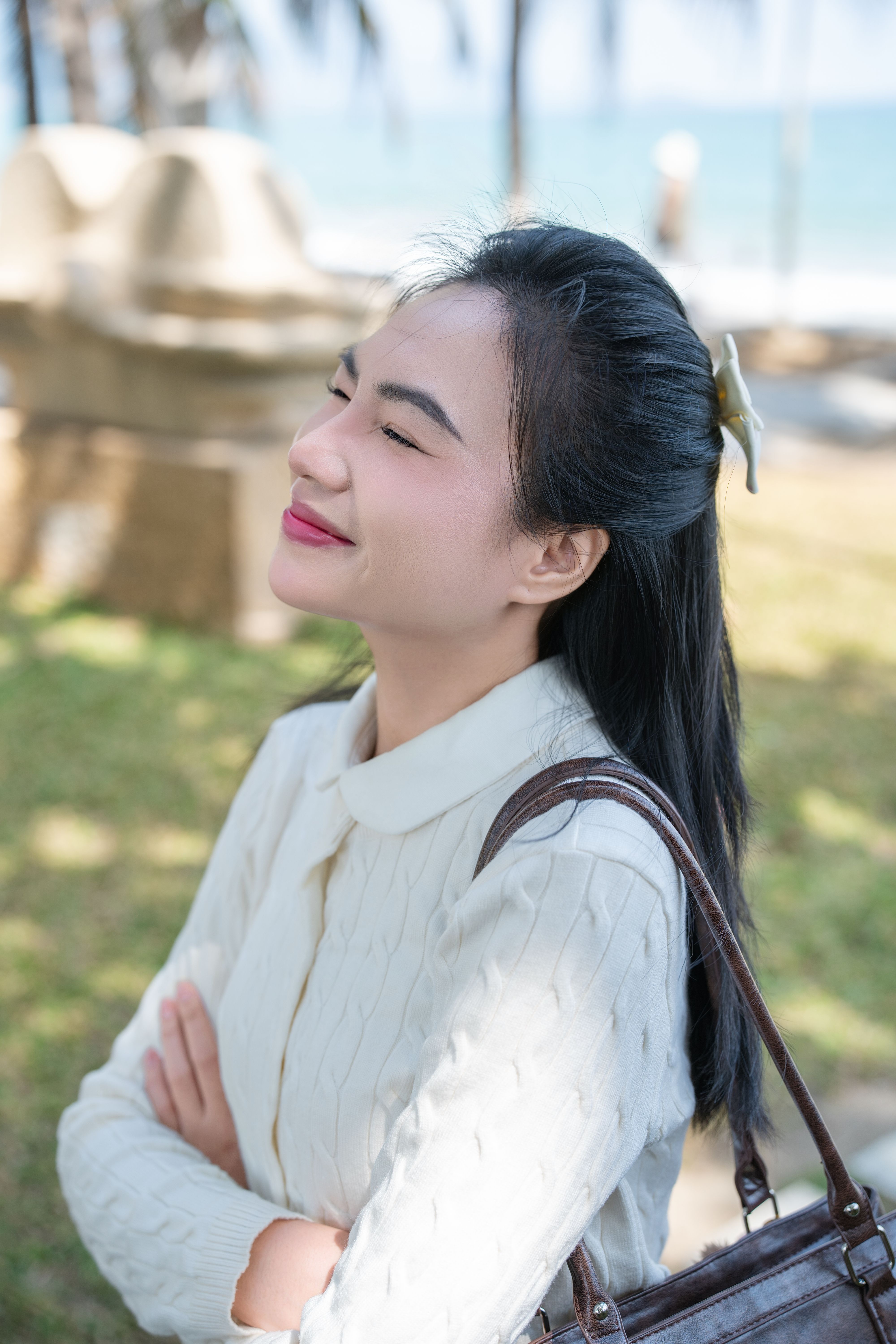A woman enjoying a sunny day at the beach, smiling with eyes closed. Serene and peaceful.