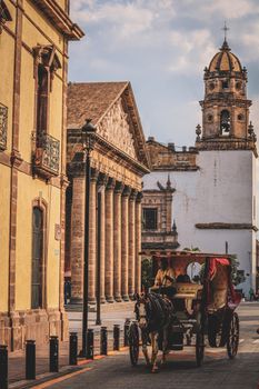 Charming scene of horse-drawn carriage by historic buildings in Guadalajara, Mexico.