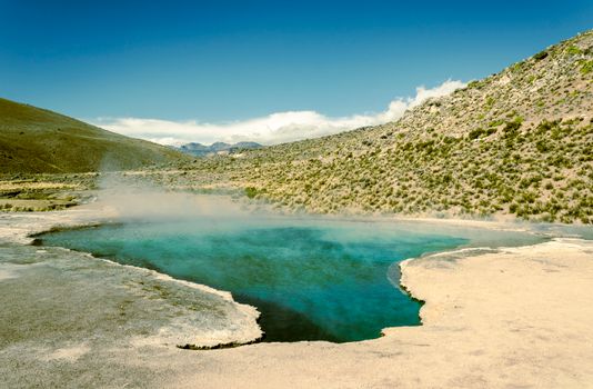 Calm hot spring amidst arid hills in Candarave, Peru with clear blue water.