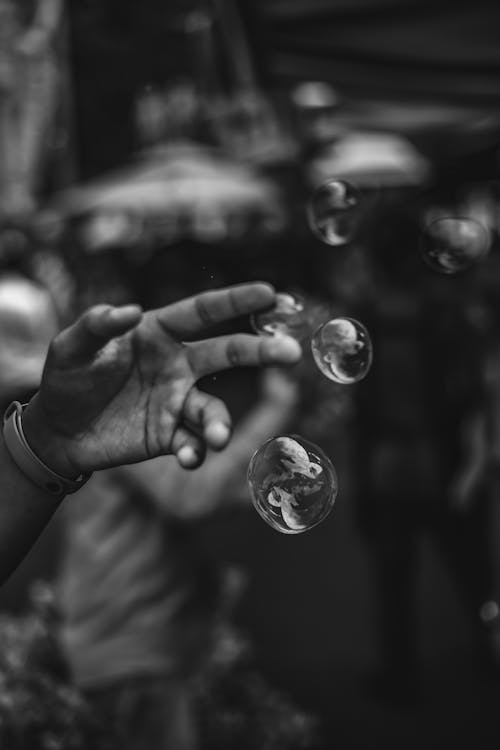 Grayscale Photo Of Person Touching Bubbles