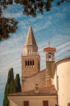 Beautiful historic stone tower with terracotta roofs and trees, under a blue sky.