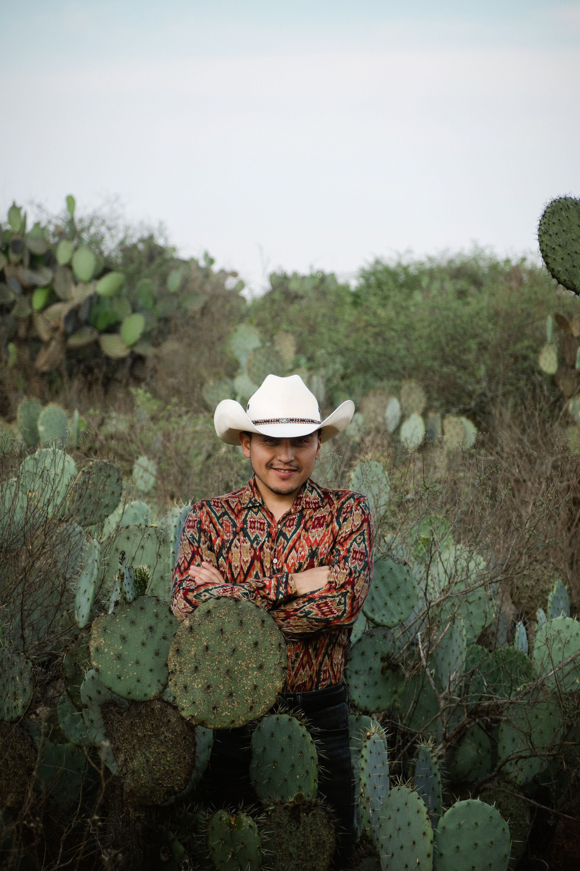 Adult male with cowboy hat in lush cactus field, embracing nature.