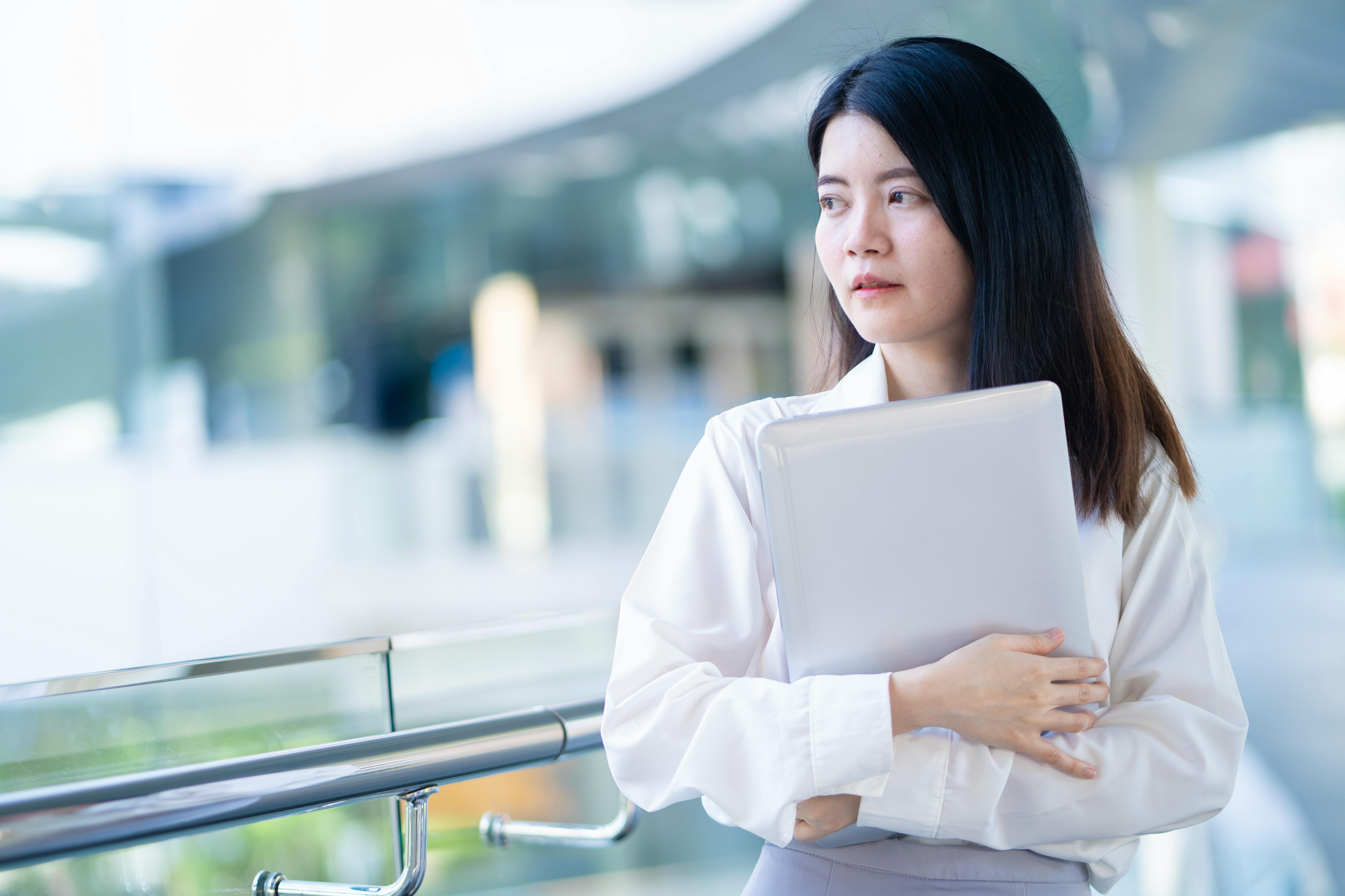 Confident young professional woman holding a laptop in a modern indoor setting.