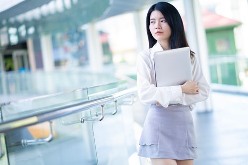Free Young Asian businesswoman holding a laptop in a modern office environment, showcasing confidence and professionalism. Stock Photo