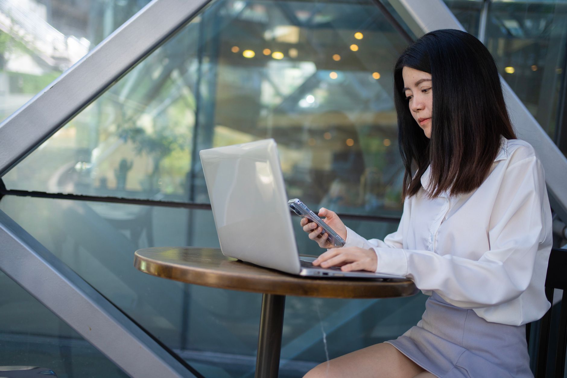 Asian woman freelancer working on laptop in a modern Bangkok cafe, capturing urban entrepreneurial lifestyle.