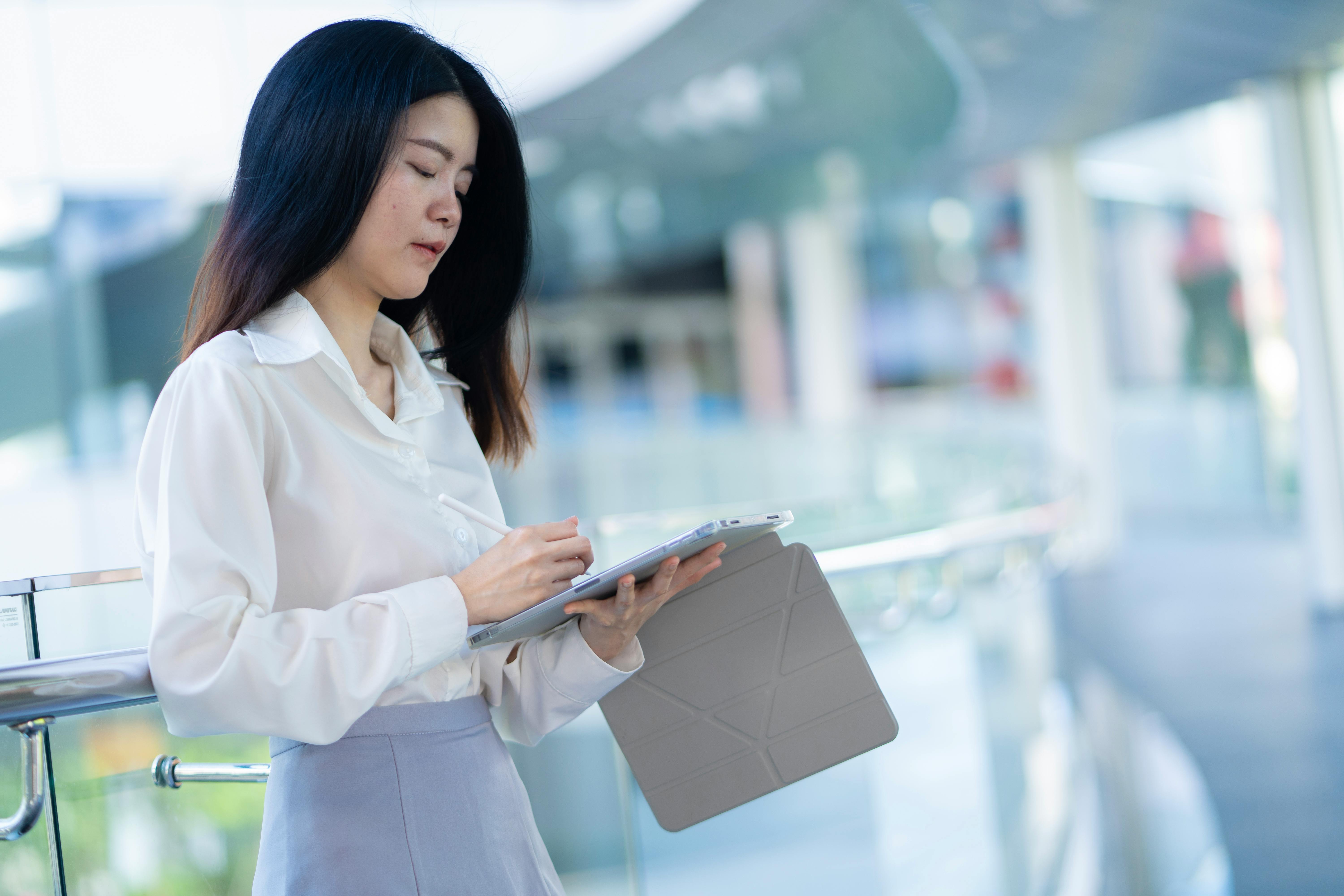 Confident Asian woman multitasking with tablet in a sleek, modern workspace.