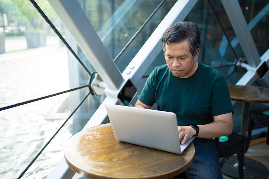 Asian man working on a laptop in a modern Bangkok café, concentrating on remote tasks.